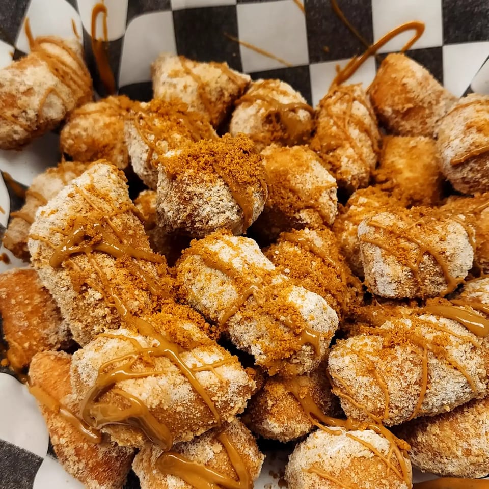 Close-up of golden-brown Italian dessert bites, drizzled with caramel and sprinkled with crumbs.