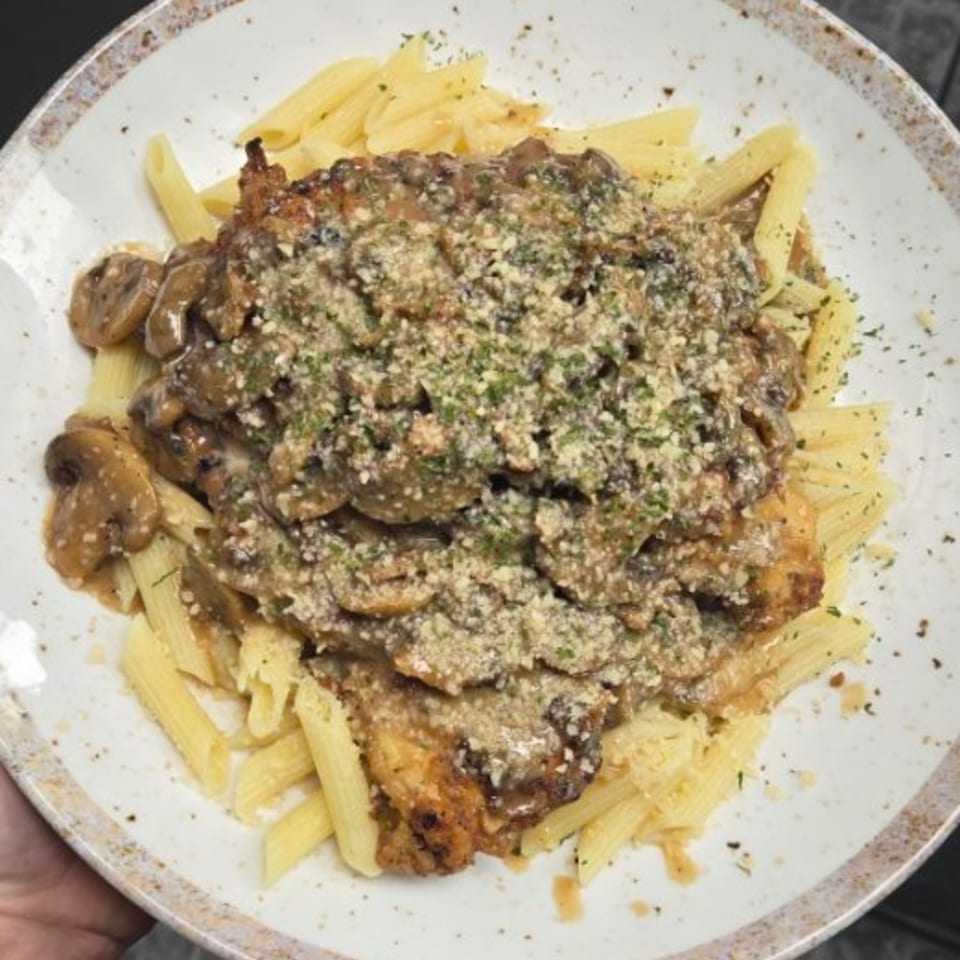 Italian penne pasta topped with chicken, mushrooms, and a creamy sauce, garnished with herbs.
