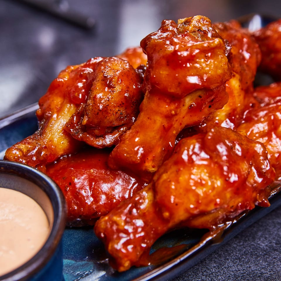 Close-up of glossy, red-sauced chicken wings on a blue plate with a side of dipping sauce.