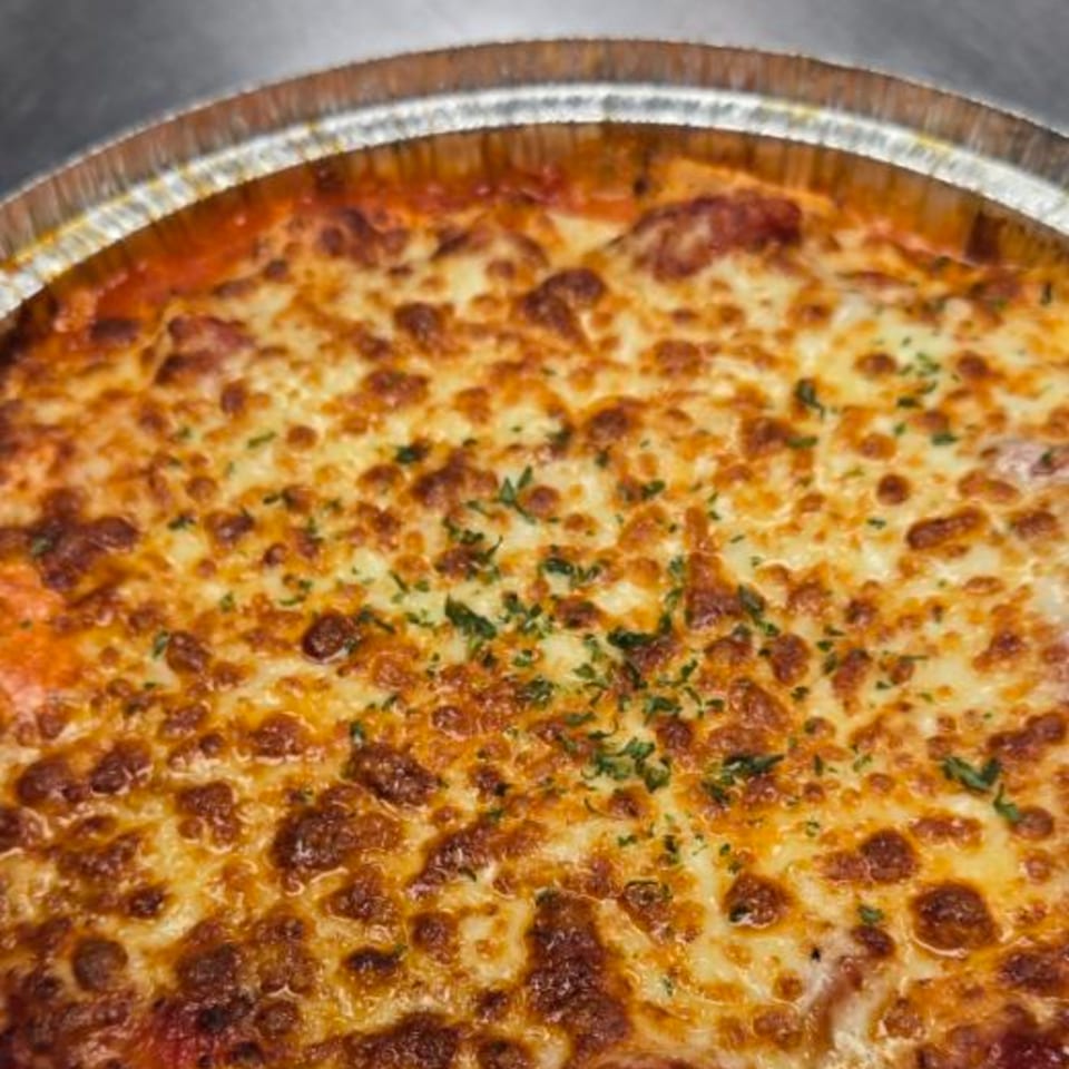 Baked Italian pasta dish with melted cheese and herbs in a foil pan.