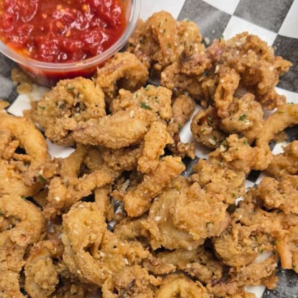 Crispy fried calamari with a side of red marinara sauce on a checkered paper liner.